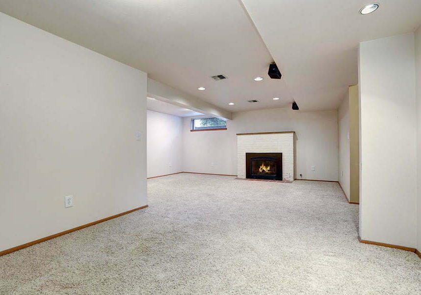 white empty basement room with fireplace and wall to wall carpet floor.